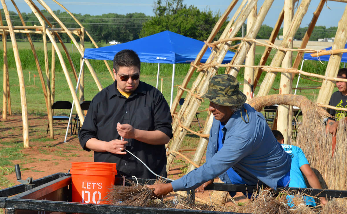 Workers prepare grass for the outside of traditional housing replicas at the Wichita Historical Center. (Wichita Tribal News)